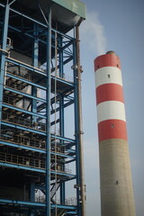 Large industrial chimney with red-white stripes and steam, beside a blue power station structure. Represents industry, energy, and potentially emissions. Suitable for themes of power generation