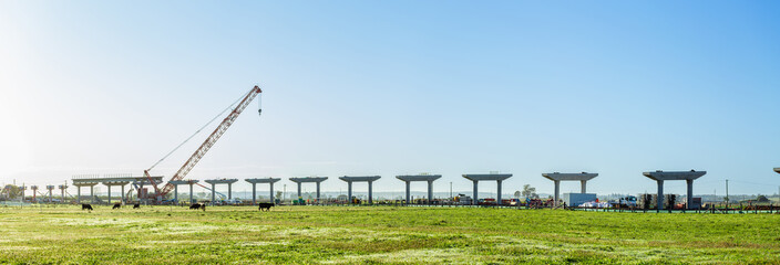 Panorama of construction site bypass road bridge being built over farmland