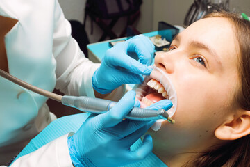 Teenage girl receiving dental cleaning with mouth retractor at clinic by dentist wearing blue gloves