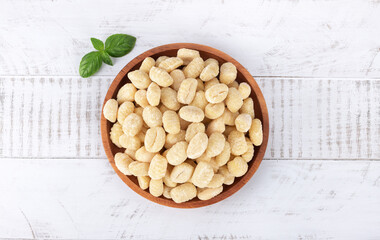 Raw Italian pasta potato gnocchi and basil on white background. Top view.