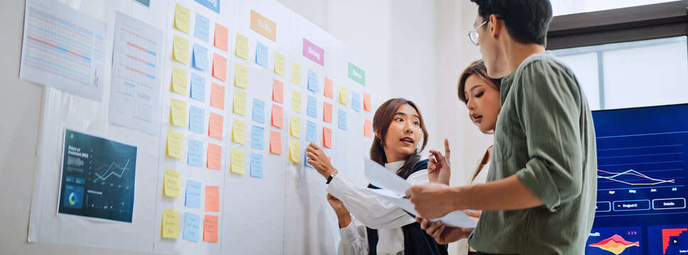 Group of Asian generation z business people work together in home office. Financial team businesspeople brainstorm meeting, use digital tablet and white board presentation. Corporate teamwork concept - Powered by Adobe