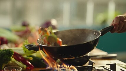 Slow-motion close up view of unrecognizable cook hand holding wok pan, tossing multicolored vegetables while frying in the kitchen