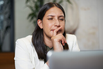 Focused Woman Deep in Thought While Looking at Laptop in Modern Office Setting
