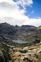 Vertical View of Laguna Grande and Jagged Peaks in Gredos Mountains with Rocky Foreground and Cloud-Draped Sky in Remote Alpine Wilderness