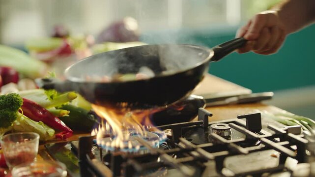 Chef tossing mixed vegetables in frying pan while flamb�ing food. Close-up shot in slow-motion