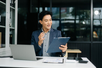 Confident businessman in suit, working on laptop and smartphone at office desk.