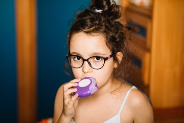 Cute little girl using asthma inhaler at home
