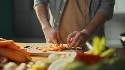Young expert chef cutting carrots on a wooden chopping board and putting them into the heated pan. Preparing vegetables in the kitchen