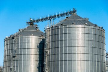 Large metallic silos designed for grain storage stand tall against a vivid blue sky, showcasing modern agricultural infrastructure and technology