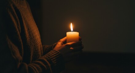 Person holding a glowing candle in a dimly lit room  