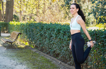 Sporty woman wearing sportswear and wireless earphones stretching legs in the park before running