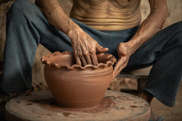 Close-up of elderly man in countryside sitting and making a pot from clay on wheel. Craftmen Asian...
