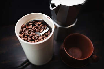 Roasted coffee beans in an electric coffee grinder on a wooden table with a moka pot and cup,...
