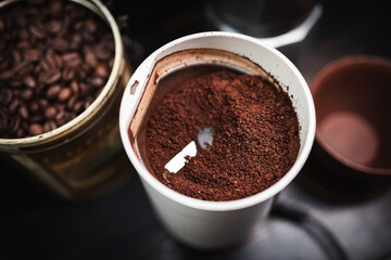 Ground coffee in an electric coffee grinder on a wooden table with a moka pot and a cup, coffee preparation