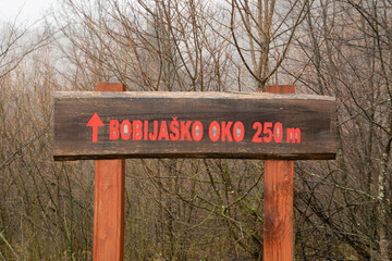 Sign on tree pointing to right to natural phenomenon lake on slopes of Grmec mountain called Bobijasko oko