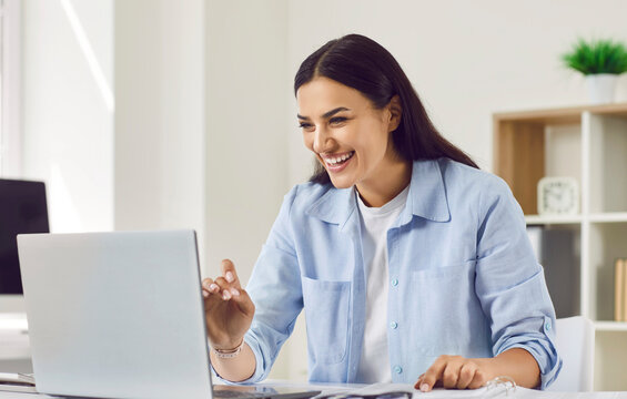 Smiling business woman sitting at the desk having video call on a laptop in the office or at home. Young happy girl working online using internet or having webinar conference or chatting online.
