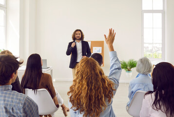 Woman sitting back on business conference raising hand to ask or answer a question on a meeting....