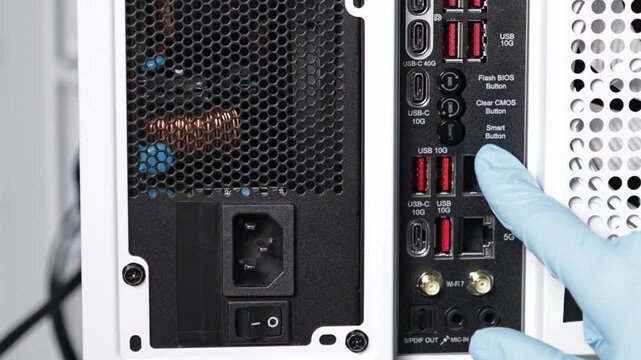 Gloved hand pointing at Clear CMOS and Flash BIOS buttons on back panel of high-end desktop motherboard with multiple USB and network ports