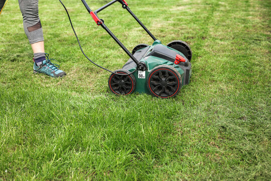 Gardening work tools. Cropped photo of gardener using modern electric aerator-scarifier for cultivation and compaction green grass lawn at backyard. Seasonal landscaping design work. Grass maintenance