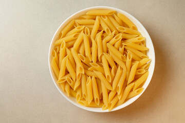 Delicious uncooked penne pasta in a white bowl ready for cooking