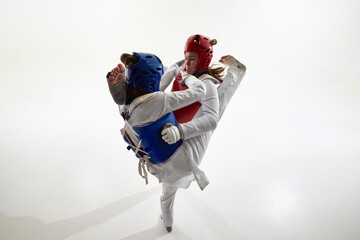 Blue and red taekwondo female athletes clashing in synchronized high kicks during dramatic studio...