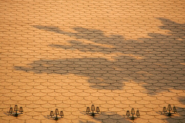 The surface is covered with an overlapping, semicircular tile pattern that casts abstract shadows....