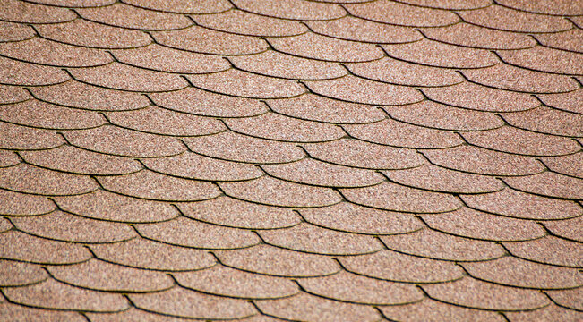 The uniform pattern of overlapping shingles creates a structured, visually appealing surface. The repeating jagged edges add a sense of rhythm and movement to the brown material.