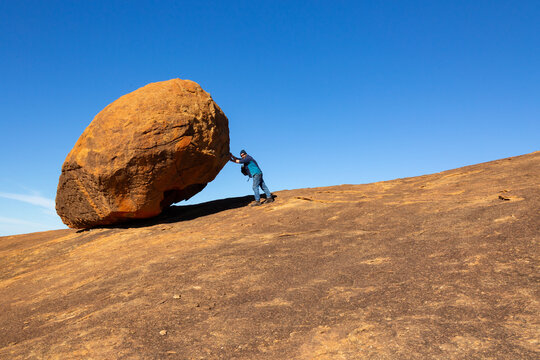 Large granite boulder dwarfs man pretending to push it