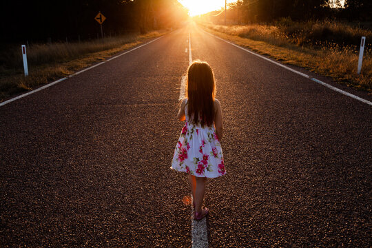 Little girl walking along the road towards the sunset light