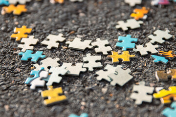 Colorful jigsaw. Unfinished scattered puzzle pieces spread on the gray asphalt pavement on the...