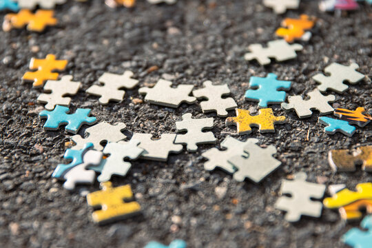 Colorful jigsaw. Unfinished scattered puzzle pieces spread on the gray asphalt pavement on the street. Messy chaotic concept. Close up. Selective focus. Blurred.