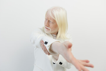 Elderly man with long white hair and light beard wearing a white suit, against a plain white...