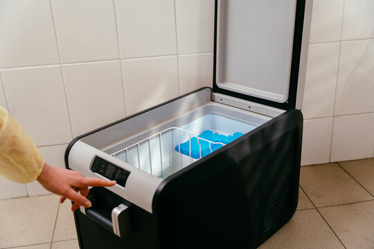 Person adjusts settings on open medical freezer with ice packs inside. Used in hospitals to store donor breast milk at precise temperature. Focus on control, hygiene, and storage safety.
