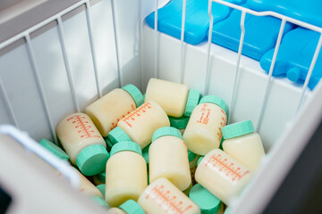 Plastic bottles with donor breast milk stored inside medical freezer alongside blue ice packs. Proper cold chain and hygienic conditions in neonatal milk bank system.