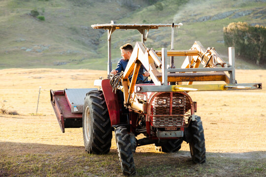 Farmer backing tractor with slasher and forklift attachments