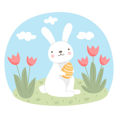 A cute white Easter bunny holds an egg in his paws on a green lawn with tulips.