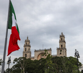 Mexico flag flying in wind at plaza grande (Merida, Yucatan peninsula) Mexican heritage state capital (famous tourist cathedral church background) colonial catholic travel tourism destination mayan
