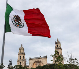 Mexico flag flying in wind at plaza grande (Merida, Yucatan peninsula) Mexican heritage state capital (famous tourist cathedral church background) colonial catholic travel tourism destination mayan
