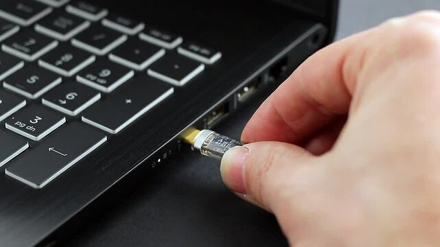 Hand connects USB Type C cable to laptop for charging and synchronizing laptop with gadgets. White cable is connected to laptop. Close-up