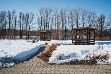 In the center of a picturesque snowy field stands a charming gazebo, surrounded by serene trees in...