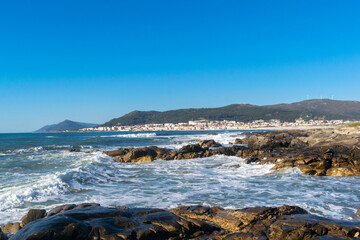 Coastal view of Vila Praia de Ancora, Portugal, with rocky shores, waves, a charming town, lush hills. A picturesque scene for travel and nature enthusiasts