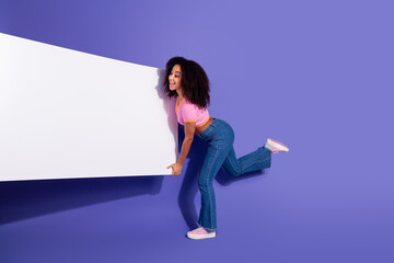 Cheerful young woman in casual attire presenting a blank white board against a vibrant purple...