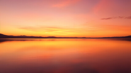 Calm lake with mountain range silhouetted against a bright orange sky. Suitable for nature themed designs, backgrounds, and out door themed marketing visuals.