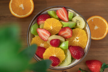 Fruit salad in bowl on wooden table. Strawberry, orange, apple, banana, kiwi healthy salad