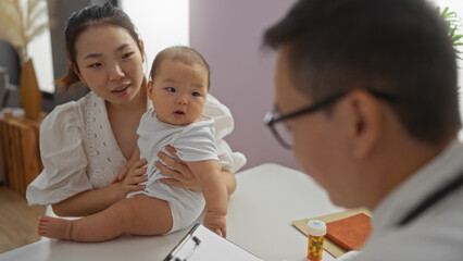 Pediatrician consulting mother and baby boy in a clinic room indoors, highlighting family warmth,...