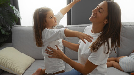 Fototapeta premium Woman and daughter share joyful moment on cozy sofa in bright living room, surrounded by warmth and love at home.