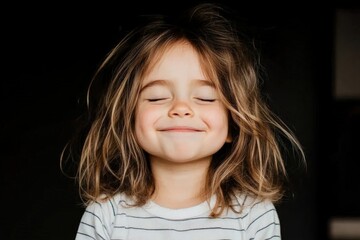 Joyful child closing eyes and smiling, showing dimples on black background