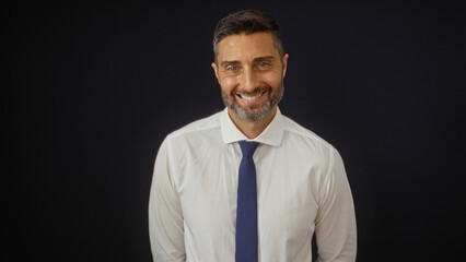 Man smiling against a black background, wearing a white shirt and tie, exuding confidence and charm, perfect for portraying business or professional themes.
