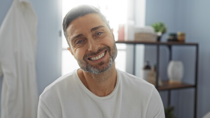 Obraz premium Handsome man smiling indoors at a spa with serene decor, wearing casual clothing, natural lighting highlighting his features, invoking relaxation and wellness.