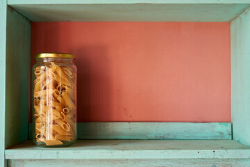 Wooden shelf displaying glass jar overflowing with penne pasta, creating warm kitchen atmosphere with rustic pantry charm
